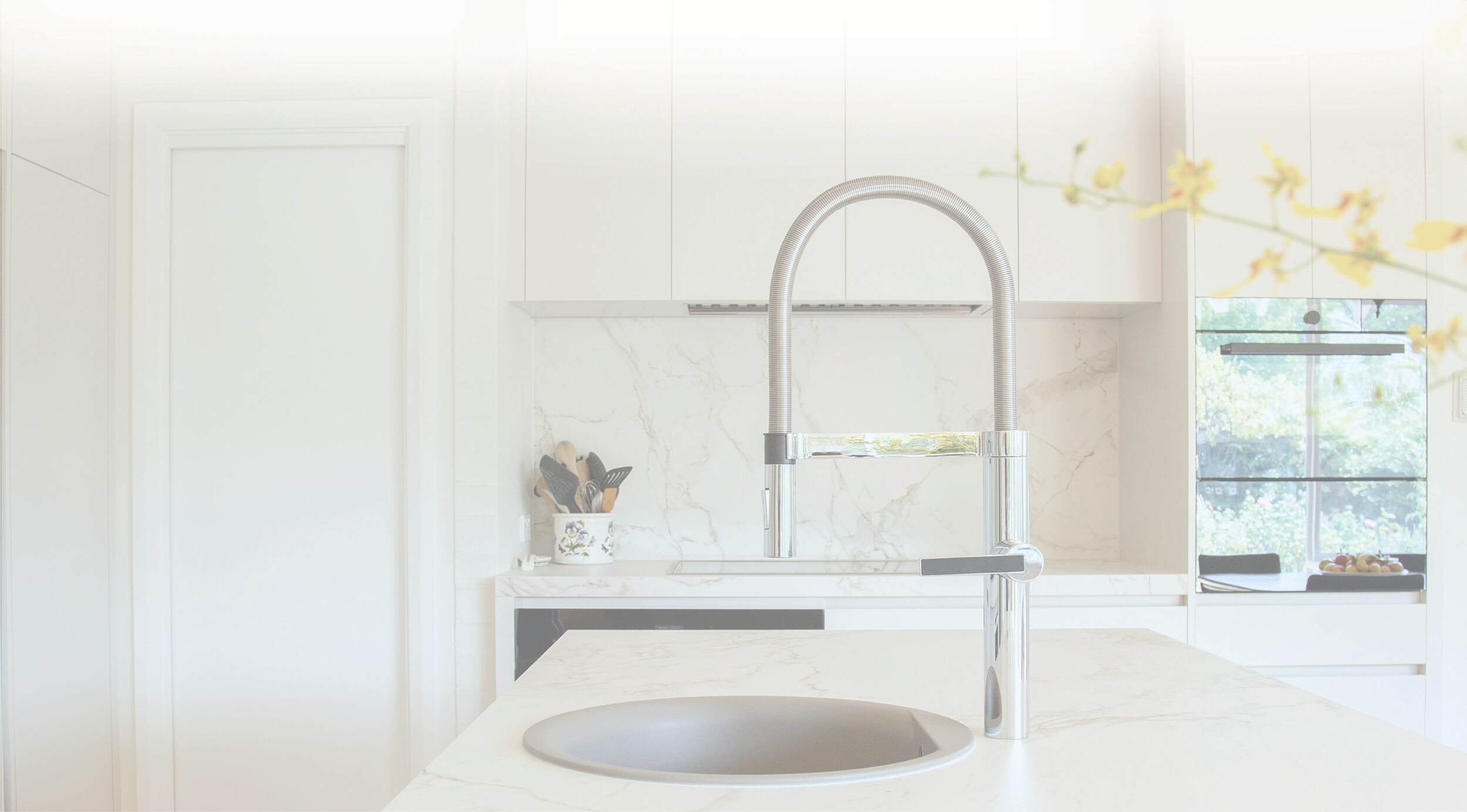 A modern kitchen scene features a chrome gooseneck faucet and round sink, set against a marble countertop and white cabinets, possibly in Coquitlam BC.
