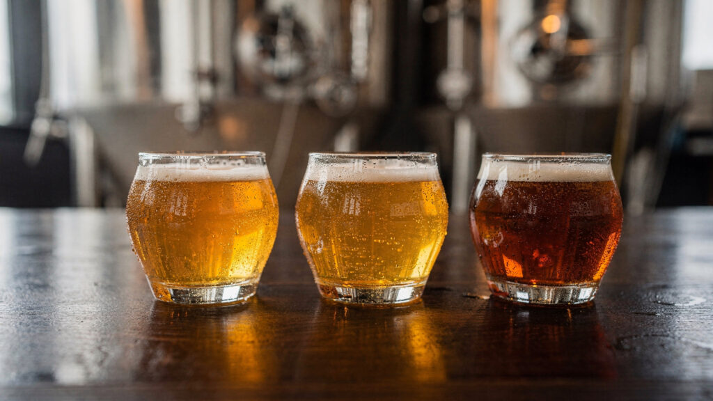 A flight of three craft beer tasting glasses on a wooden bar top in a Coquitlam area brewery taproom